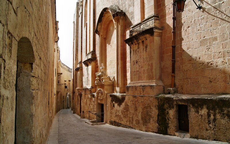 Schmale, historische Gasse in Mdina, Malta, mit alten Sandsteinmauern und beeindruckender Architektur.