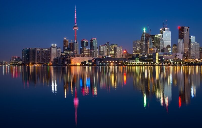 Toronto Skyline bei Nacht mit leuchtendem CN Tower und farbenfrohen Reflexionen im Ontariosee.