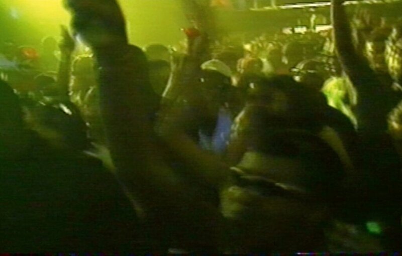 Low-light VHS capture of rave crowd dancing at night under green lighting
