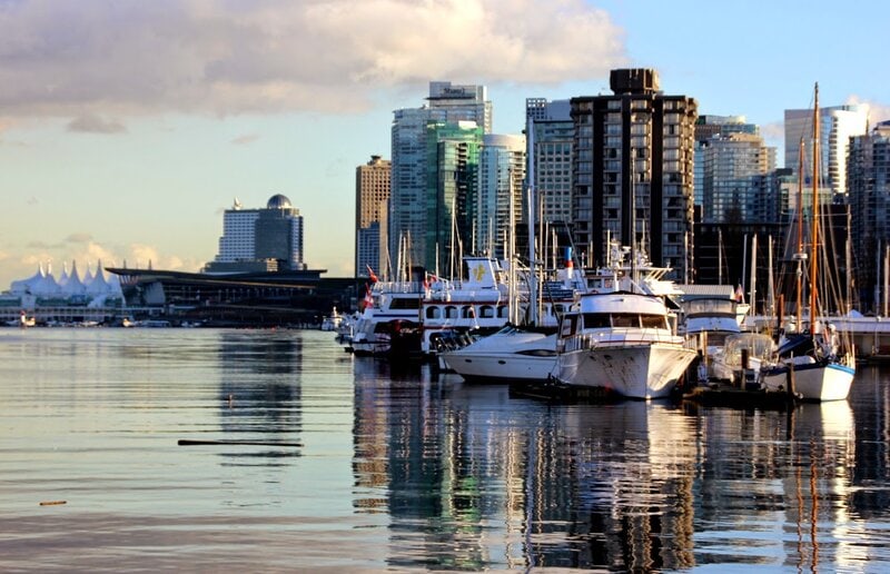 Yachthafen in Vancouver mit luxuriösen Booten, reflektierendem Wasser und moderner Skyline im Hintergrund.