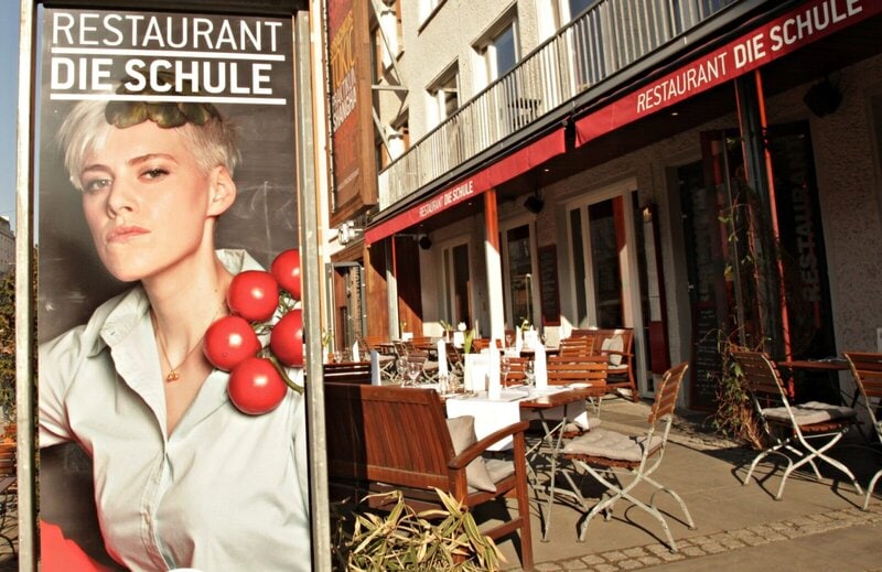 Restaurant „Die Schule“ mit Außenbereich und Werbeplakat im Sonnenschein in Berlin