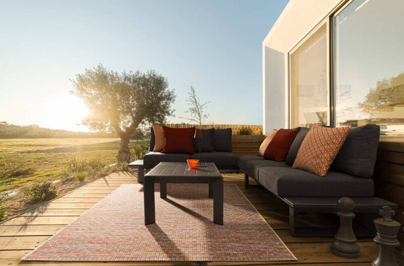 Soggiorno all'aperto con divano e cuscini sulla terrazza al tramonto, atmosfera rilassante.