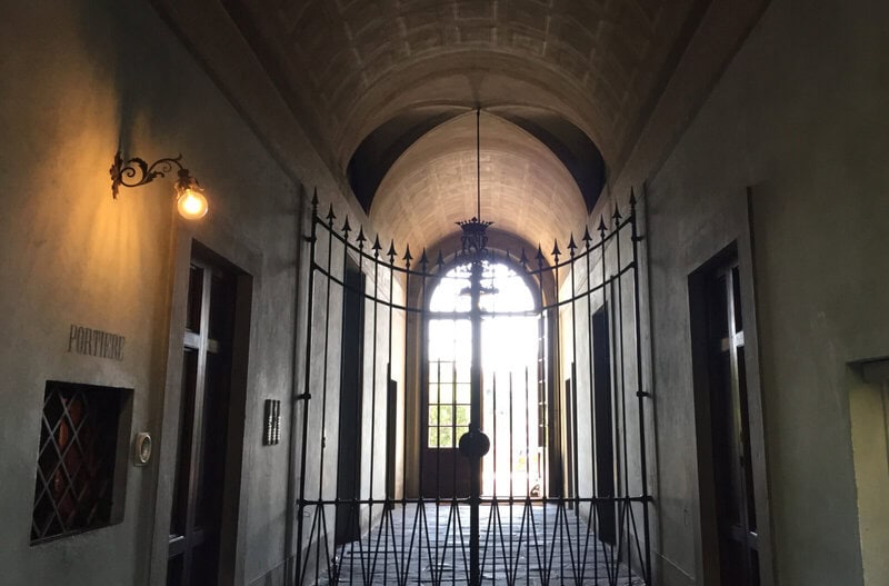 Historischer Eingangsbereich mit gewölbter Decke, schmiedeeisernem Tor und nostalgischer Beleuchtung.