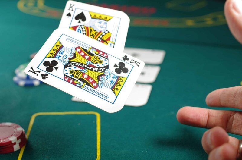 A hand flips two cards onto a green table in a gambling context