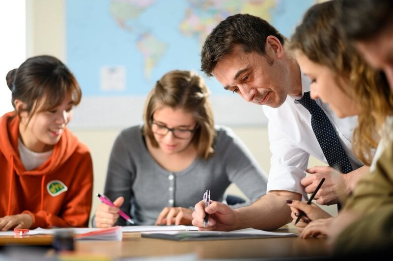 Engagierter Englischlehrer unterstützt internationale Studierende bei einer Schreibaufgabe in LSI Portsmouth.