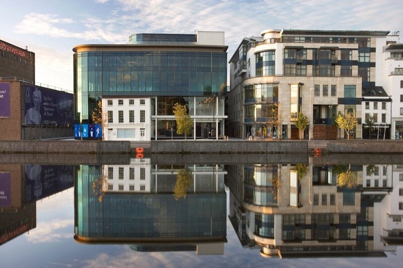 Moderne Glasgebäude mit Spiegelung im ruhigen Fluss in Cork, Irland.