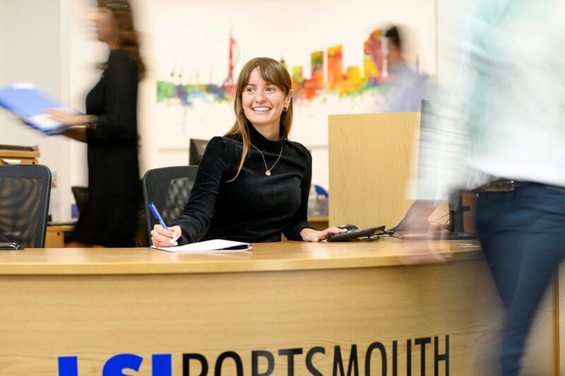 Freundliche Empfangsmitarbeiterin an der Rezeption von LSI Portsmouth begrüßt Studierende.
