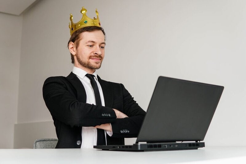 Self-confident arrogant businessman with golden crown on head using laptop.