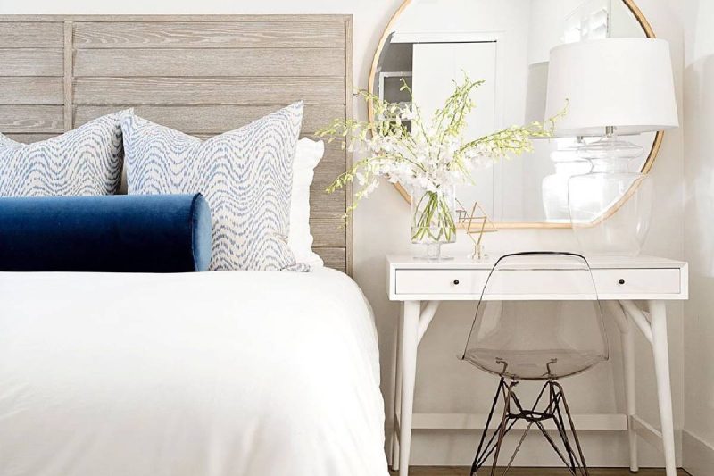 Bright, modern bedroom with elegant bedside table, stylish mirror, and fresh floral accents.