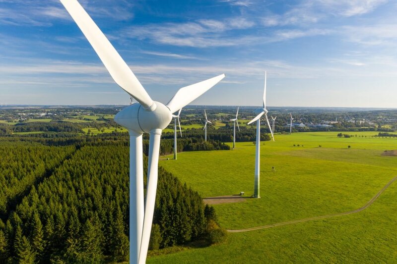 Aerogenerador visto de cerca en parque eólico rodeado de bosque y campo verde, energía renovable IELO