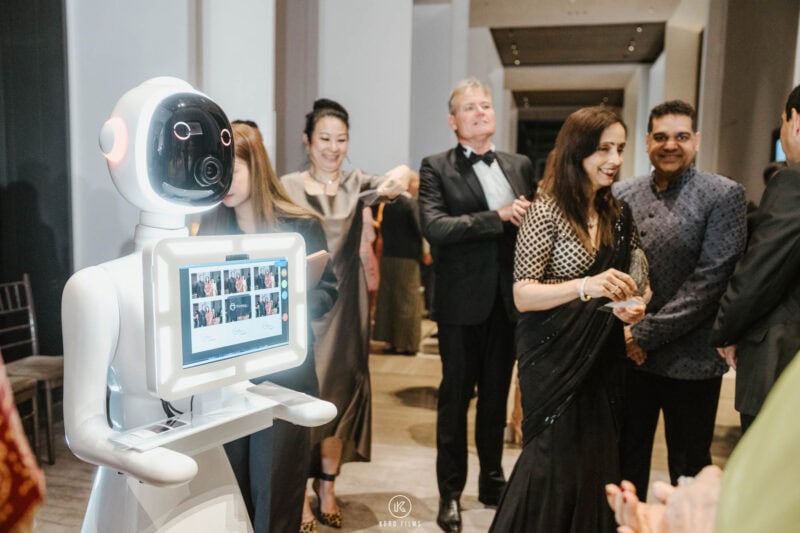 Robot photo booth showing a guest's photo on its screen as wedding guests mingle