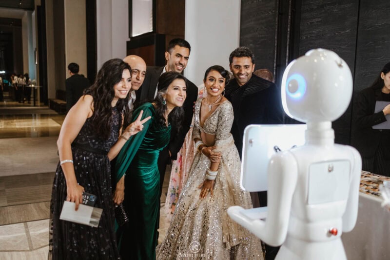Bride and her friends posing with the white robot photo booth at a wedding reception