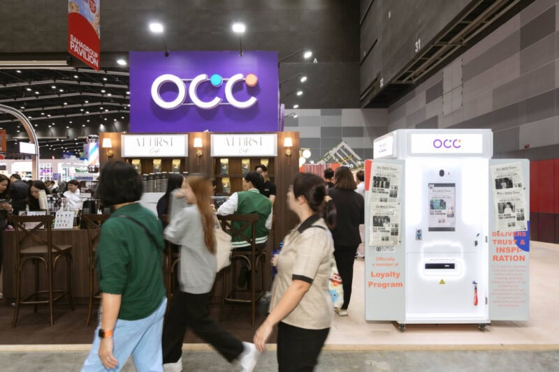 Visitors walking past a branded newspaper photo booth in a busy exhibition hall in Bangkok