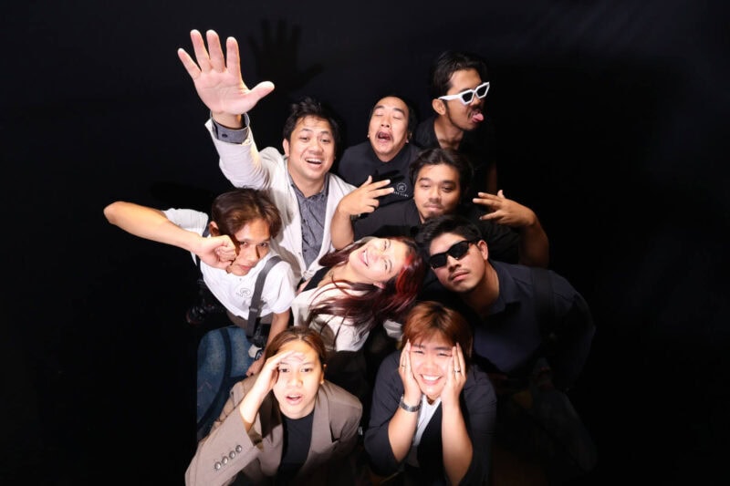 Top view photo booth group photo: nine guests pose and wave up at the overhead camera on a black backdrop