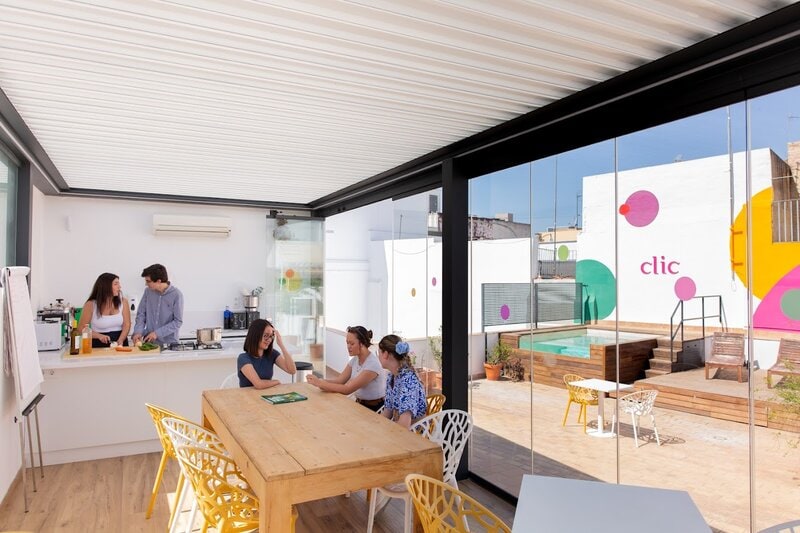 Junge Menschen kochen und unterhalten sich in der modernen Dachterrassenküche der Sprachschule clic Sevilla, mit Blick auf Pool und bunte Wandgestaltung.