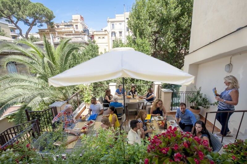 Sprachschüler genießen eine entspannte Lernatmosphäre auf einer sonnigen Terrasse mit mediterranem Flair.