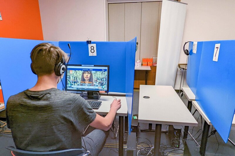 Ein Student mit Kopfhörern sitzt in einer Prüfungsstation mit Trennwänden und arbeitet am Computer.