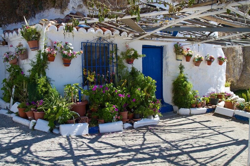 Weißes, traditionelles Haus in Andalusien mit blauen Fenstern und Tür, dekoriert mit bunten Blumentöpfen