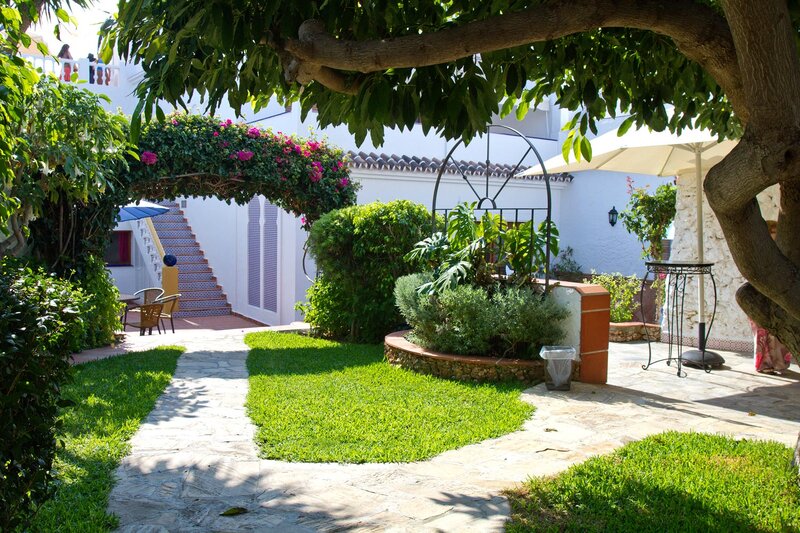 Mediterraner Garten der Sprachschule in Nerja mit blühendem Torbogen, Natursteinweg und Sitzplätzen im Schatten