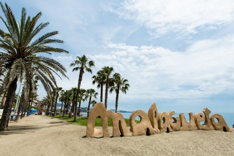 Palmen gesäumter Strand mit dem bekannten „Malagueta“-Schriftzug am Playa de La Malagueta in Málaga