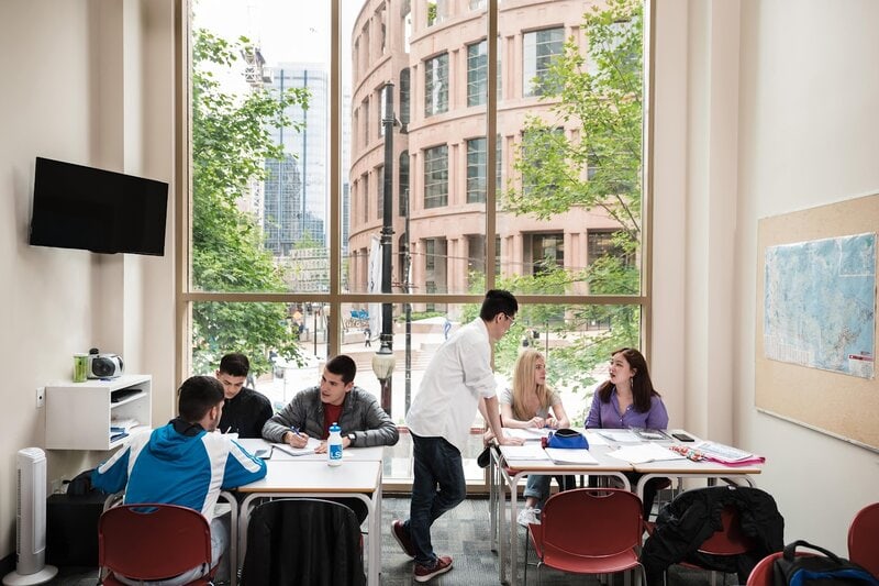 Studierende in einem modernen Klassenraum mit großen Fenstern und Blick auf die Vancouver Public Library.