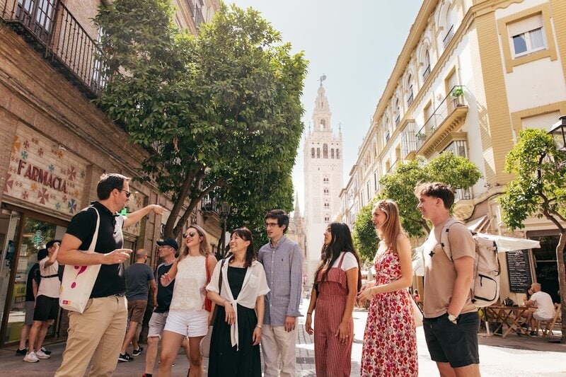 Gruppe junger Sprachschüler mit Guide bei einer Stadtführung durch das historische Zentrum mit Blick auf die Giralda in Sevilla