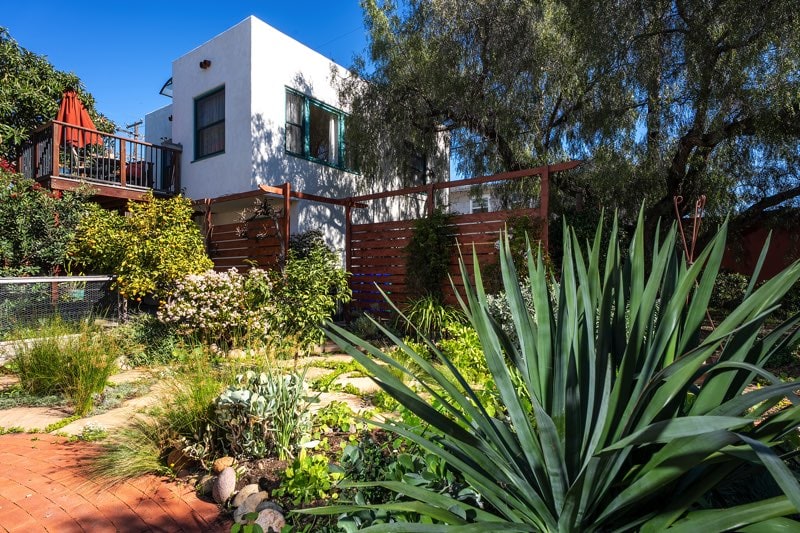 Lush backyard garden at 3237-39 Dale St in North Park, featuring Mediterranean-style succulents, a brick pathway, and the detached two-story casita with a private upper-level deck overlooking mature trees.