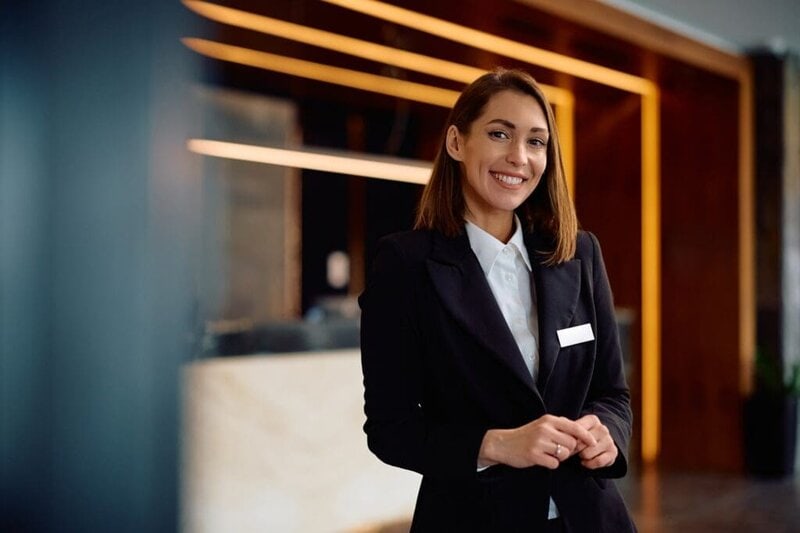 Happy female concierge in hotel hallway looking at camera.