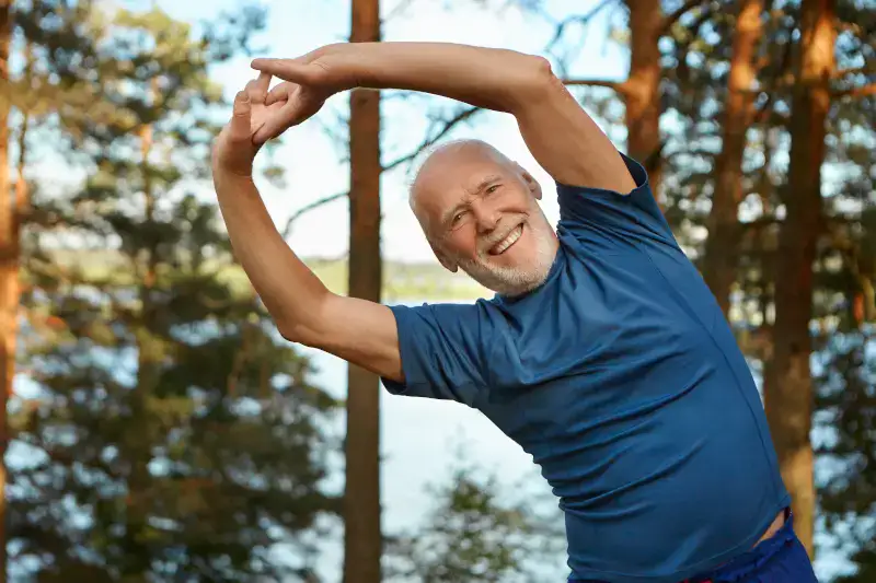 Older man stretching outdoors in a natural setting, promoting healthy lifestyle and fitness for seniors.