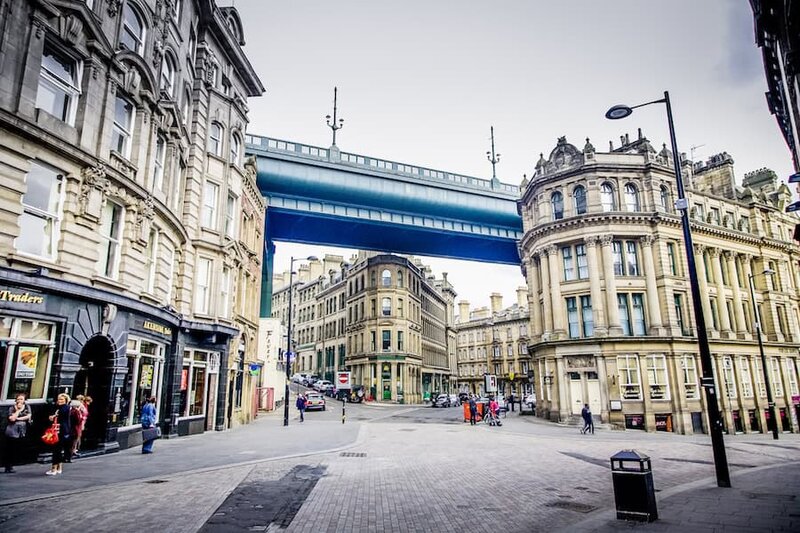 City street with historic buildings and a blue bridge overhead.