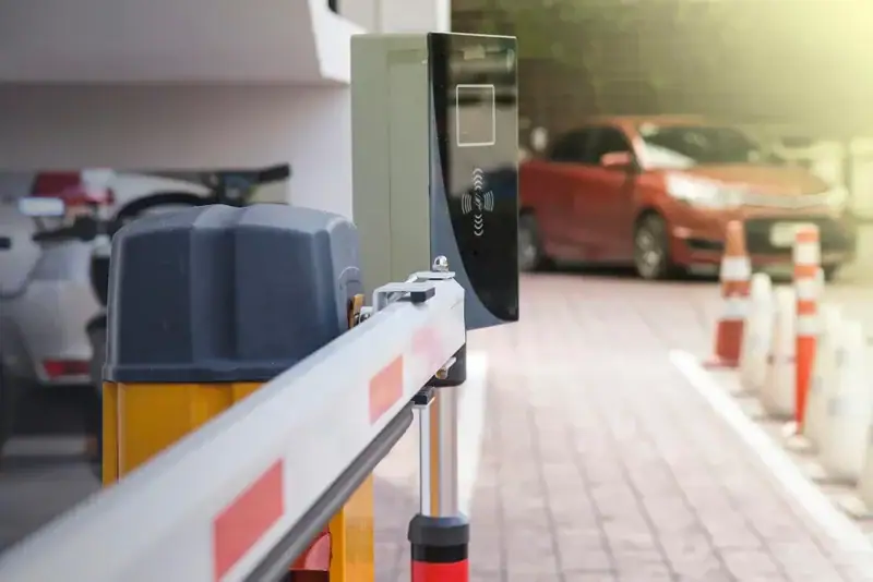 Sistema de controle de acesso com cancela e leitor de cartão em estacionamento com carro vermelho ao fundo. Conteúdo sobre Pedágio free flow São Paulo