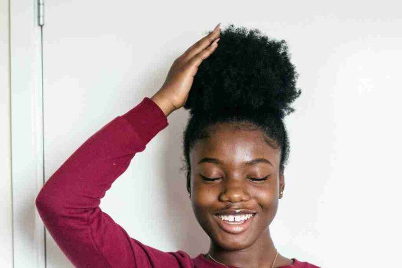A Black woman touching her hair and smiling, embodying the lightness that trauma therapy in Farmington Hills can restore.