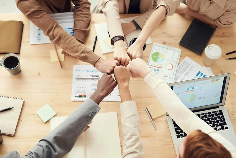 Vue du dessous d'un groupe de collègue qui réunissent leur poing au centre de la table
