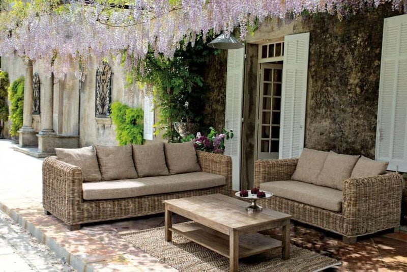 Soggiorno esterno con divani in vimini e decorazioni floreali in giardino.