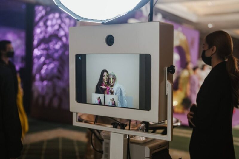 Event host standing next to the studio photo booth while its screen shows a guest photo