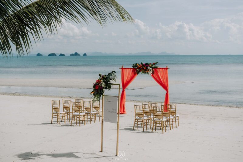 Gold chairs and a red draped arch set up for a beach wedding ceremony at Baan Puri, Koh Samui
