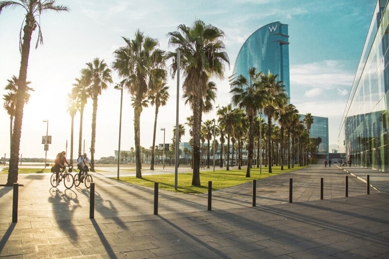 Sonnenuntergang an einer modernen Strandpromenade mit Palmen, Radfahrern und dem markanten W-Hotel im Hintergrund.