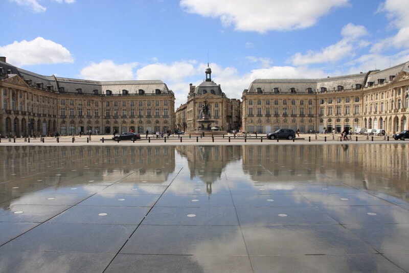 Place de la Bourse in Bordeaux mit der Spiegelung im Miroir d'eau bei blauem Himmel.