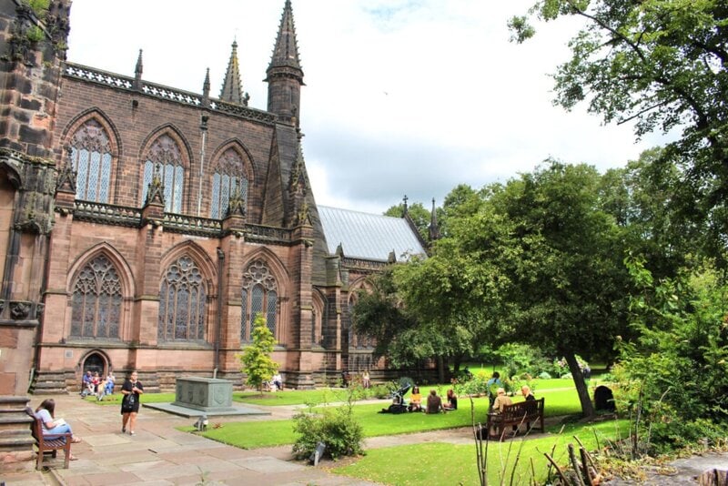 Die Chester Cathedral mit ihrem beeindruckenden gotischen Baustil und dem ruhigen, grünen Garten, in dem Menschen entspannen.