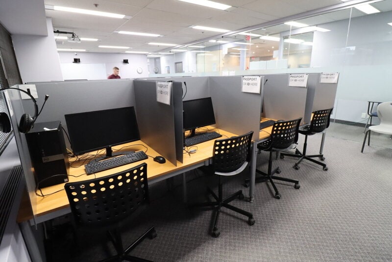 Ein modernes Prüfungs- oder Testzentrum mit abgetrennten Computerarbeitsplätzen, ausgestattet mit Headsets und Monitoren.