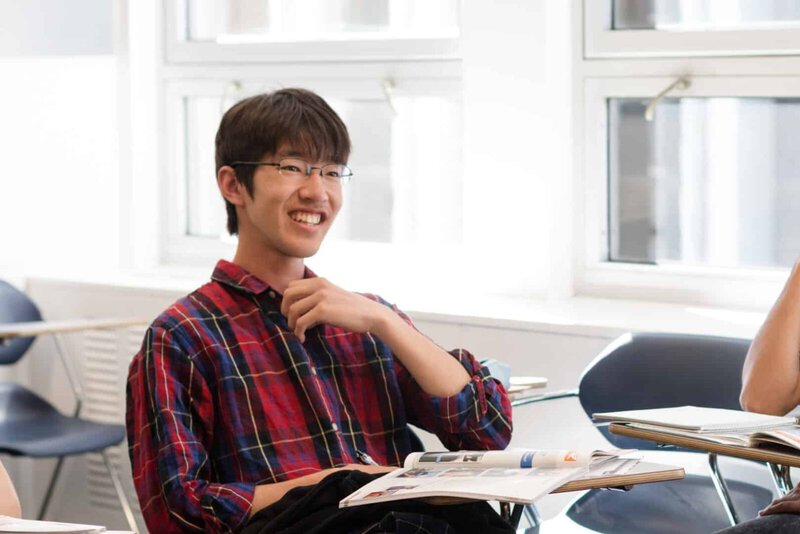 Ein lachender Student in einem modernen, hellen Klassenzimmer mit Lernmaterialien auf dem Schreibtisch.