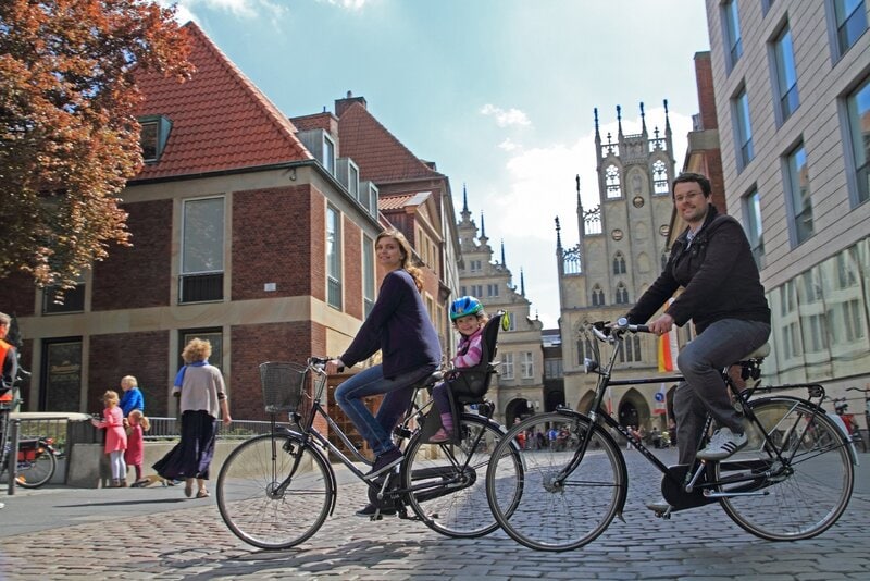Familie fährt Fahrrad durch historische Altstadt mit Kopfsteinpflaster und gotischer Architektur