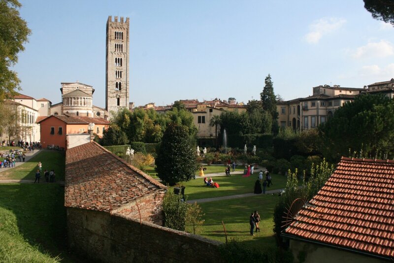 Historischer Garten mit Statuen und Springbrunnen in Lucca, Italien, mit einem markanten Glockenturm im Hintergrund.