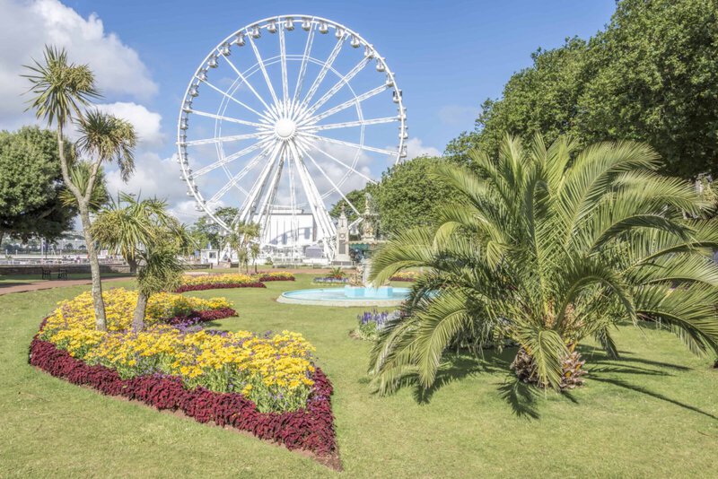 Riesenrad in Torquay mit blühenden Gärten und Palmen im Vordergrund.