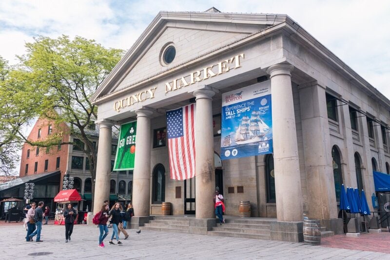 Historischer Quincy Market in Boston mit amerikanischer Flagge und belebtem Vorplatz.