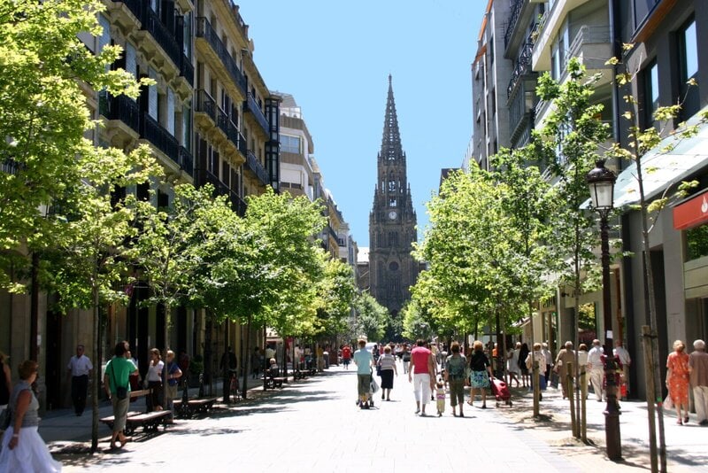 Fußgängerzone in San Sebastián mit Bäumen und Blick auf die neugotische Kathedrale del Buen Pastor
