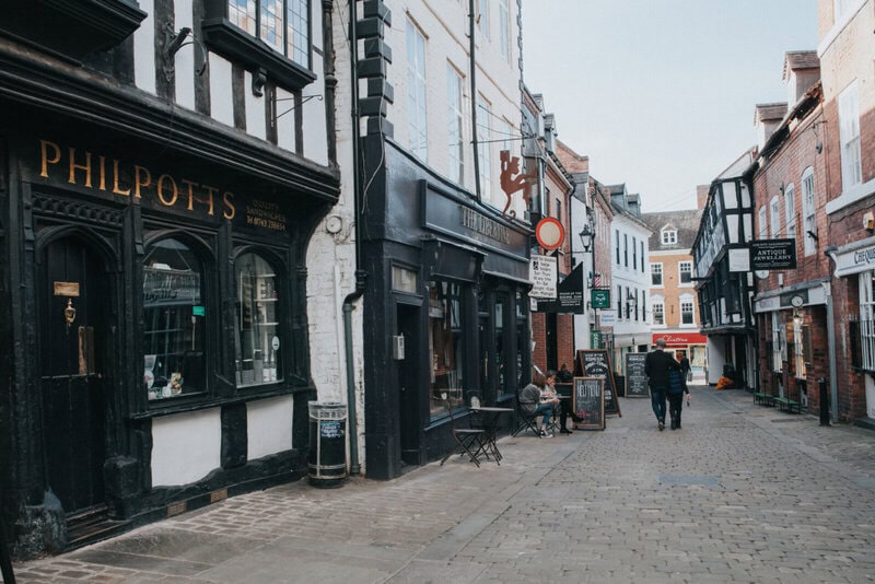 Historische Kopfsteinpflasterstraße in Shrewsbury mit Fachwerkhäusern, kleinen Geschäften und Cafés.