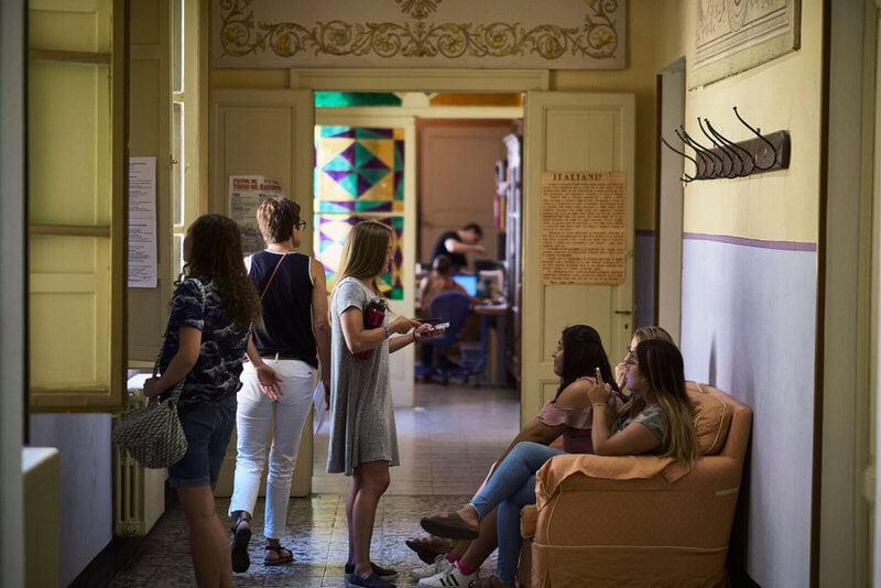 Studenten in einem historischen Flur einer Sprachschule in Italien, während sie sich unterhalten und auf den Unterricht warten.