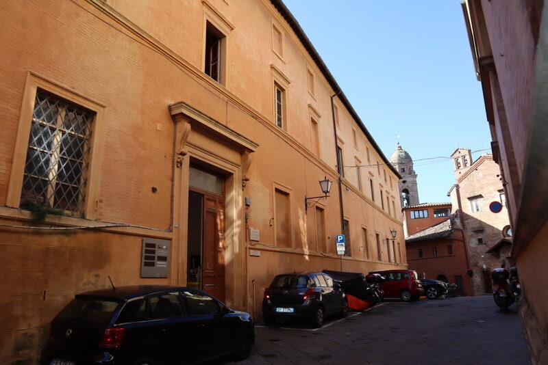 Historisches Gebäude mit orangefarbener Fassade in einer engen Straße mit parkenden Autos in Italien.
