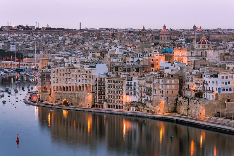 Beleuchtete historische Gebäude und Hafen in Birgu (Vittoriosa), Malta, bei Sonnenuntergang.